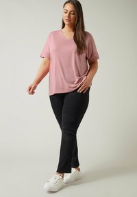 Rosa kortärmad V-ringad topp som är kombinerad med svarta tajta jeans och vita sneakers. Tyget verkar mjukt och slätt med en avslappnad passform.