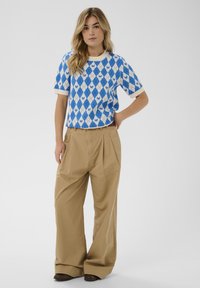 Kék-fehér rombuszmintás kötött rövid ujjú ing krémszínű szegéllyel, laza fazonú khaki nadrággal párosítva. Barna cipő.