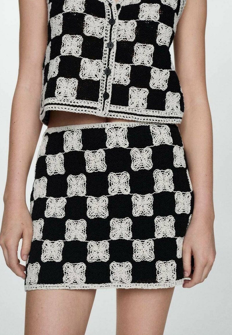 Ensemble deux pièces au crochet noir et blanc avec motifs floraux carrés à carreaux, comprenant un top sans manches boutonné et une mini-jupe.