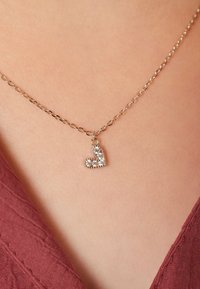 Zilverkleurige ketting met een klein harthanger, versierd met heldere kristallen, tegen een effen huidachtergrond.