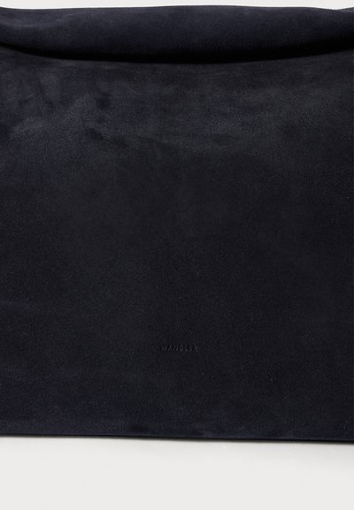 Tumši zila zamšādas soma ar gludu tekstūru, minimālistisku dizainu un rollētu augšpusi. Apakšā ir izspiežams zīmola nosaukums.