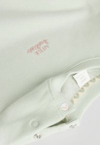 Pull en coton vert clair avec texte brodé en rose, col côtelé et fermeture à boutons, texture lisse et doublure à motifs.