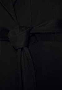 Avvolgimento in tessuto nero con dettaglio della cintura annodata, caratterizzato da una texture morbida e una finitura liscia, che crea un aspetto elegante e aderente.