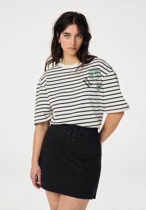 Gestreept t-shirt in crème en zwart met een ronde halslijn en losse pasvorm, met een geborduurd ontwerp. Gecombineerd met een zwarte spijkerrok met vetersluiting.