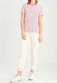 Polo tričko s červenými a bílými pruhy, krátké rukávy a výstřih na tři knoflíky, spárované s bílými zkrácenými džíny a bílými teniskami.