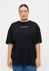 Camisa oversized negra de algodón, con mangas cortas y el texto "Day Dreamer" bordado en púrpura en el pecho.
