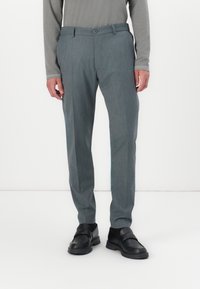Lichtgrijze broek met een subtiele textuur, rechte snit en een knопsluiting. Gdraagd met zwarte instapschoenen.