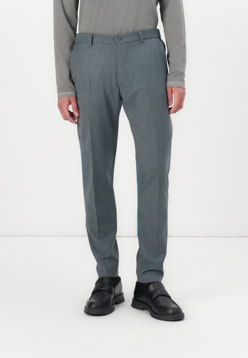 Lichtgrijze broek met een subtiele textuur, rechte snit en een knопsluiting. Gdraagd met zwarte instapschoenen.