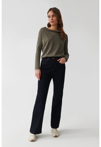Blugi din denim oscur albastru, cu un design evazat, asortați cu un top lung cu mânecă, de culoare verde deschis, care are un guler înclinat și mâneci strânse.