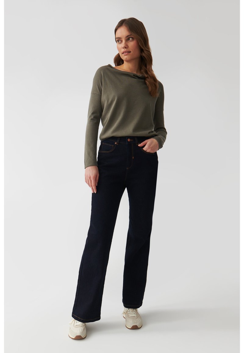 Jeans in denim blu scuro con un design svasato, abbinati a un top a maniche lunghe verde chiaro con scollo a caramella e maniche aderenti.