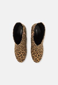 Bottines imprimé léopard avec une base beige et des accents noirs, présentant une fermeture éclair latérale et une texture lisse. Le design comprend des tiges arrondies.