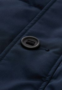 Donkerblauwe gewatteerde jassen stof met een ronde zwarte knop met een gat en een bevestigde koord, gladde textuur en gestikte naden.