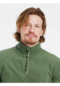 Pullover in pile verde con colletto alto, mezza zip frontale e dettagli con logo. Tessuto morbido con cuciture in evidenza e un emblema sul petto.