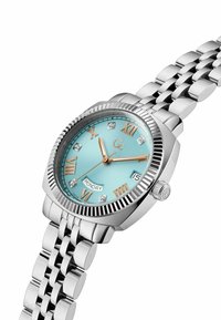 Reloj de pulsera redondo de plata presenta un dial turquesa con números romanos, acentos de diamante y una correa de metal pulido. Incluye un display de fecha y día.