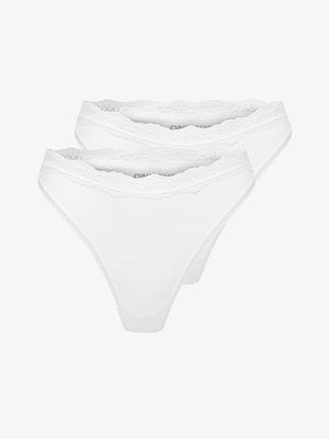 Młoda kobieta o długich ciemnych włosach, ubrana w biały top z koronkowymi wykończeniami i pasujące majtki, pozująca z ręką na biodrze.