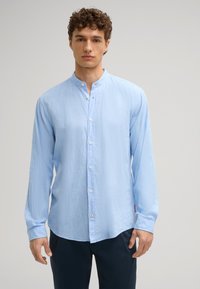 Camicia azzurro chiaro con colletto alla cinese, dotata di maniche lunghe e vestibilità rilassata. Tessuto testurizzato e dettaglio discreto della patta frontale.