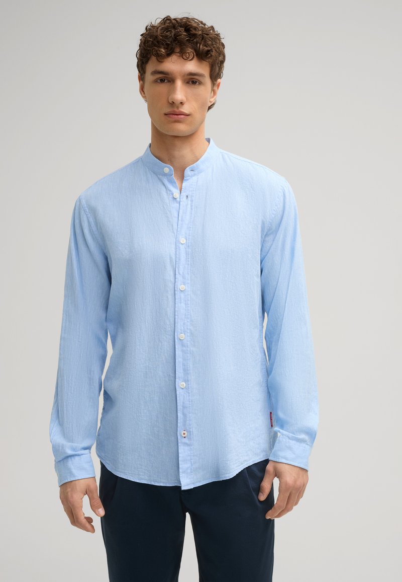 Camicia azzurro chiaro con colletto alla cinese, dotata di maniche lunghe e vestibilità rilassata. Tessuto testurizzato e dettaglio discreto della patta frontale.