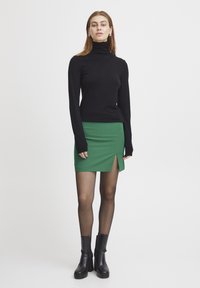 Pulover negru cu guler înalt asortat cu o fustă mini verde ajustată, care prezintă o despicătură pe lateral. Modelul poartă colanți transparenți și botine negre cu toc.