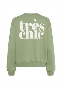 Zelená mikina s bielym textom "très chic" na chrbte. Má okrúhly výstrih, rebrované manžety a voľný strih. Mäkká textúra látky.