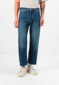 Jeans de mezclilla azul claro con corte recto, que presentan un diseño clásico de cinco bolsillos y un acabado ligeramente desvanecido. Llevados con zapatillas crema.