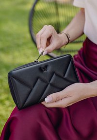 Black leather wallet with a geometric, quilted design and a zipper closure. Smooth texture highlighted by a subtle logo.