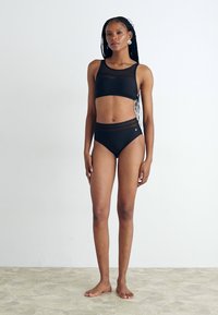 Juodas dviejų dalių maudymosi kostiumėlis, pagamintas iš lygaus audinio. Jame yra prigludusi crop top bliuskutė su juostele ir kelnaitės aukštu liemeniu su subtiliu emblem. 