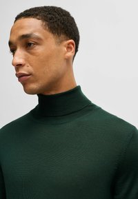 Donkergroen coltrui gemaakt van geribbelde brei stof, met een aangesloten ontwerp en hoge kraag. Glad textuur met minimale details.