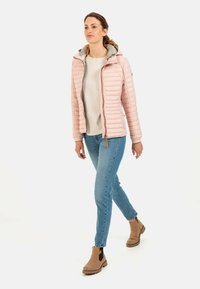 Lys pink quiltet jakke med hætte, parret med en beige bluse og blå jeans. Jakken har en frontlynlås og ribbede manchetter.