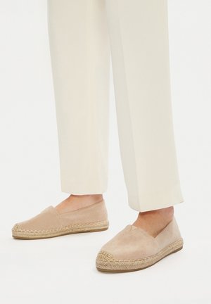 Beżowe espadryle z zamszu z plecioną podeszwą z jutowego sznurka i zaokrąglonym noskiem. Prosty design bez zapięć, zestawione z jasnymi spodniami.