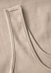 Camiseta sin mangas de color beige con una textura acanalada, escote redondeado y costuras reforzadas en los bordes. Tejido suave con un acabado liso.