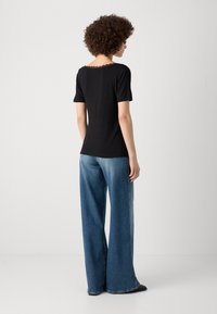 Top nero a maniche corte con scollatura in pizzo testurizzato, abbinato a jeans in denim azzurro chiaro dalla vestibilità ampia. Design semplice e contemporaneo.