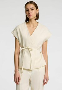 Ivory linnen wikkeltop met korte mouwen, een v-hals en een stoffen strik rond de taille. Zachte textuur en ontspannen pasvorm.