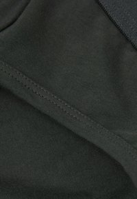 Dunkelgrüner Stoff mit glatter Textur, der an den Kanten sichtbare Nähte aufweist. Das Material wirkt dehnbar und leicht.