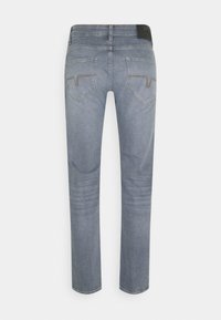 Jean en denim bleu clair vu de dos avec deux poches cousues et une étiquette de marque noire sur la ceinture.
