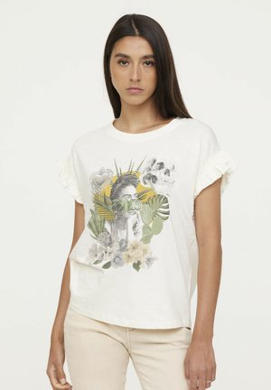 T-shirt de couleur crème avec des manches volantes, présentant un design graphique d'une femme entourée de verdure et d'éléments floraux.