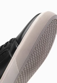 Baskets en cuir noir avec une semelle en caoutchouc texturée et des accents blancs, mettant en avant un bout arrondi et un motif de traction détaillé.