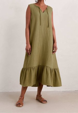 Robe midi sans manches vert olive en tissu texturé avec un ourlet volanté, portée avec des sandales plates marron à brides sur une personne debout.