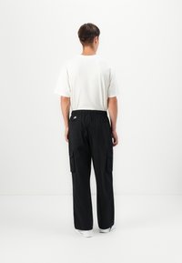 Black cargo pants with an elastic waistband, two side pockets, and a relaxed fit. Paired with a plain white short-sleeve t-shirt.