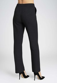 Pantaloni neri su misura con una texture liscia e taglio dritto, dotati di tasche laterali e una cintura comoda, abbinati a tacchi neri.