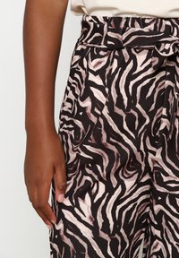 Black and pink zebra-patterned pants with a belted waist, smooth texture, and tapered legs. Visible hand resting on the side.