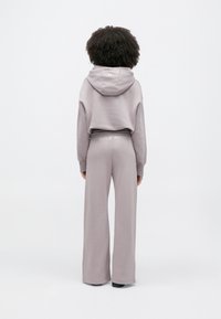 Ανοιχτό μωβ cropped φούτερ με κορδόνια και ασορτί φαρδιά φόρμα. Το ύφασμα φαίνεται απαλό με λεία υφή· η μέση διαθέτει λογότυπο.