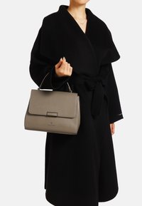 Borsa a mano in pelle grigia con un design strutturato, forma rettangolare, manico superiore e chiusura a scatto. Indossata con un abito nero.