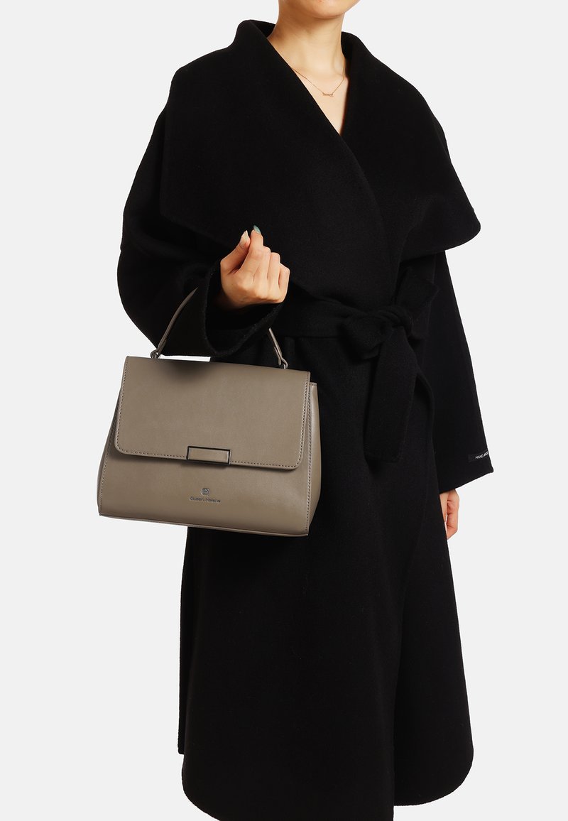 Borsa a mano in pelle grigia con un design strutturato, forma rettangolare, manico superiore e chiusura a scatto. Indossata con un abito nero.