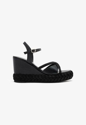 Sandalia de cuña negra con plataforma trenzada y tiras delgadas. Ajuste con hebilla; textura suave y diseño angular. Construida para la estabilidad.