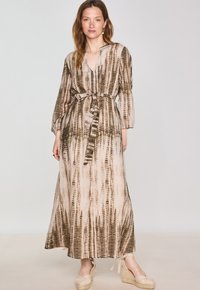 Lungo vestito di colore neutro con cintura in vita, scollatura a V e maniche lunghe; presenta un motivo testurizzato marrone e beige.