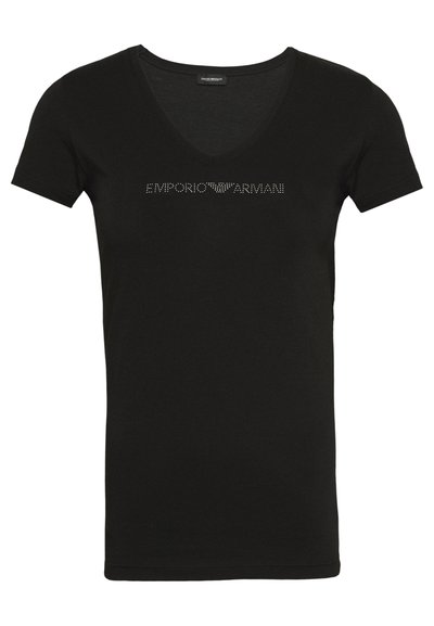 Camiseta negra de manga corta con escote en V. Presenta "EMPORIO ARMANI" en tachuelas metálicas a lo largo del pecho. Textura de tela suave.