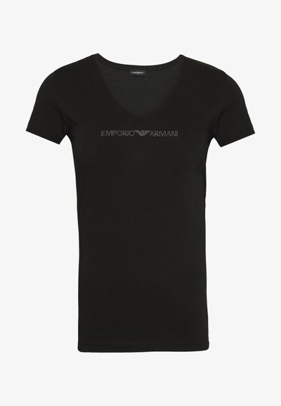 Camiseta negra de manga corta con escote en V. Presenta "EMPORIO ARMANI" en tachuelas metálicas a lo largo del pecho. Textura de tela suave.