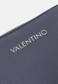 Valentino logo on textured dark blue fabric with a smooth, metallic finish. The material appears durable and woven.
