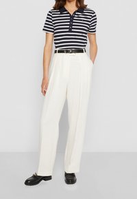 Gestreepte polo in marineblauw en wit, gecombineerd met hooggesneden, wijde crèmekleurige broeken. Een zwarte riem en schoenen maken de look compleet.