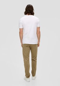 Weißes Baumwoll-T-Shirt mit kurzen Ärmeln, kombiniert mit hellbraunen Cordhosen und weißen Turnschuhen, von hinten betrachtet.